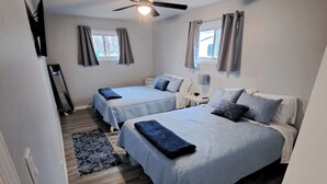 A bedroom with two beds, a ceiling fan, a window with curtains, and a small bedside table. - Beautifully remodeled house that sleeps 10 by Lake Erie Fun. (Sandusky)