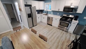 A modern kitchen with white cabinets, stainless steel appliances, and a wooden dining table. - Beautifully remodeled house that sleeps 10 by Lake Erie Fun. (Sandusky)