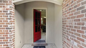A red door leading into a room with a white door frame and a welcome mat at the entrance. - Charming 3-bedroom house located minutes from LSU (Baton Rouge)