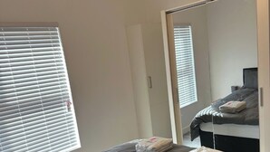 A bedroom with a bed, a large mirror, and a window with blinds.
