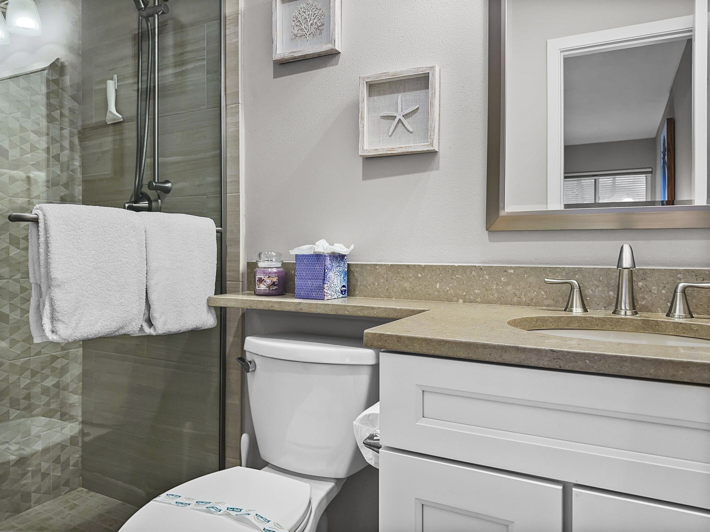 Une salle de bain avec une douche à parois de verre, des toilettes blanches, un meuble-lavabo et un miroir.