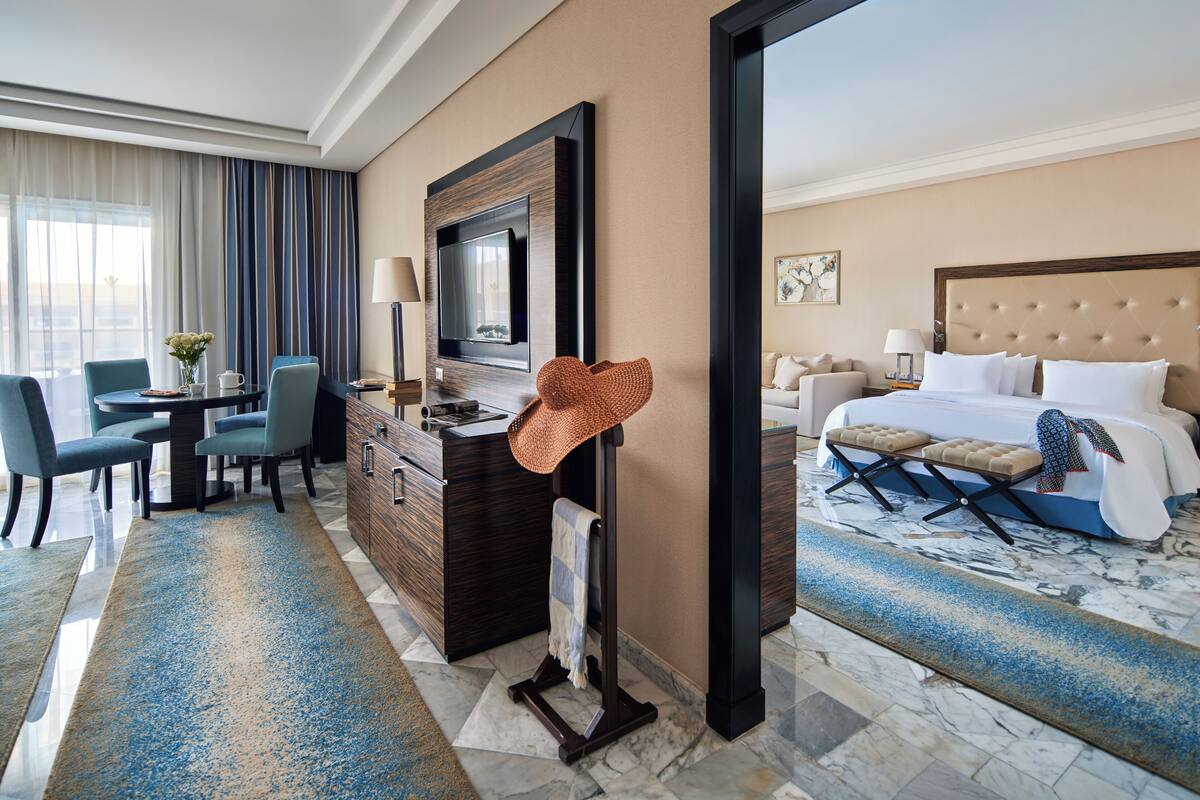 A hotel room with a bed, a desk with a chair, a television, and a large window with curtains.