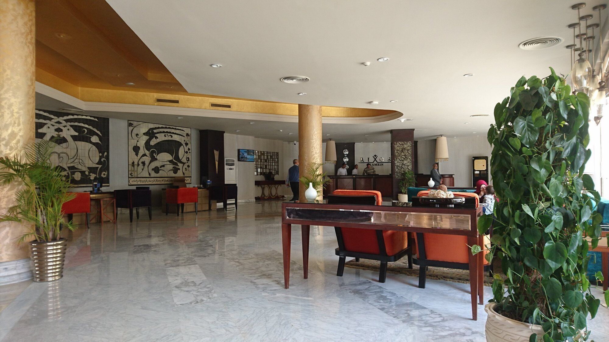 A spacious lobby with marble flooring, a reception desk, seating areas, and a large decorative plant.