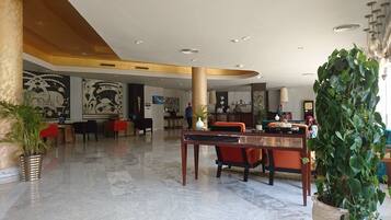 A spacious lobby with marble flooring, a reception desk, seating areas, and a large decorative plant.