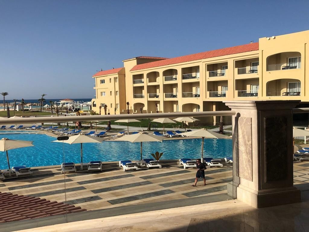 A hotel with a swimming pool, lounge chairs, and umbrellas.