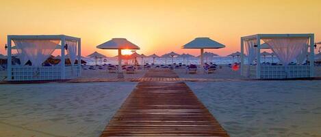 A beach with a wooden walkway leading to beach umbrellas and cabanas.