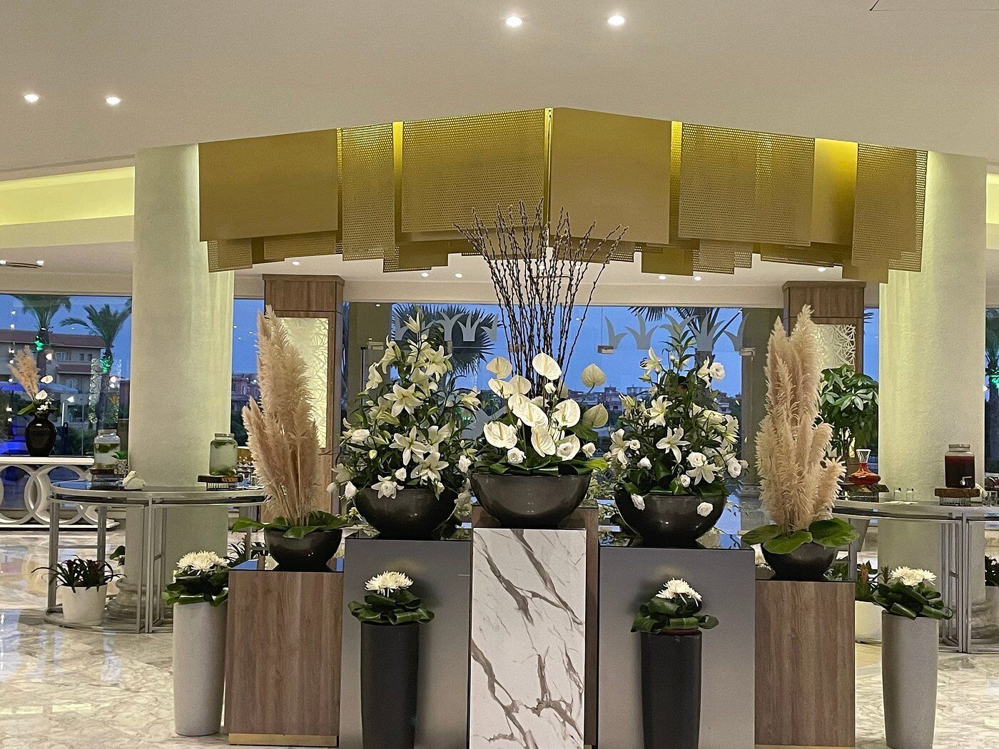 Un área de recepción con un mostrador, varios arreglos florales y un diseño arquitectónico moderno con una pared de acento amarilla.