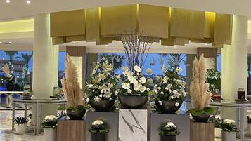 Un área de recepción con un mostrador, varios arreglos florales y un diseño arquitectónico moderno con una pared de acento amarilla.