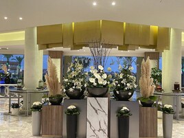 Un área de recepción con un mostrador, varios arreglos florales y un diseño arquitectónico moderno con una pared de acento amarilla.