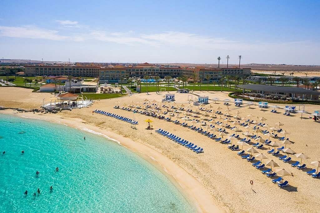 Un resort en la playa con una piscina grande, tumbonas y un edificio al fondo.