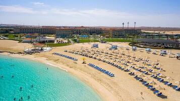 Un resort en la playa con una piscina grande, tumbonas y un edificio al fondo.