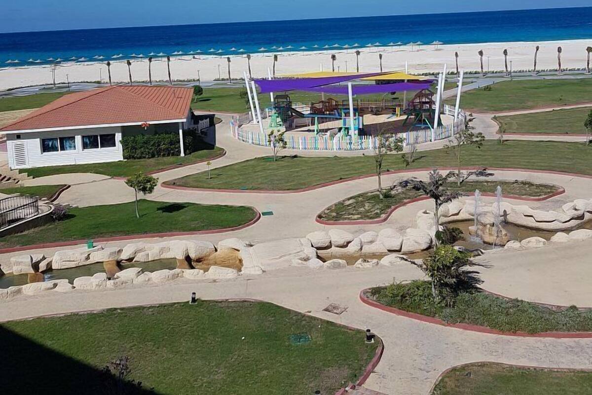 A coastal resort with a beach, a playground, and a building with a red roof.