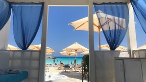 A beachside room with a view of the beach, featuring a bed, a chair, and a table. - Ghazala Luxury Collection Alamein (El Alamein)