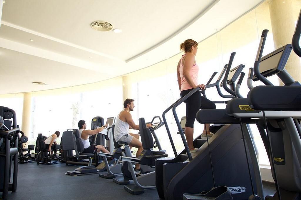 A gym with treadmills and weight machines, large windows, and a curved ceiling.