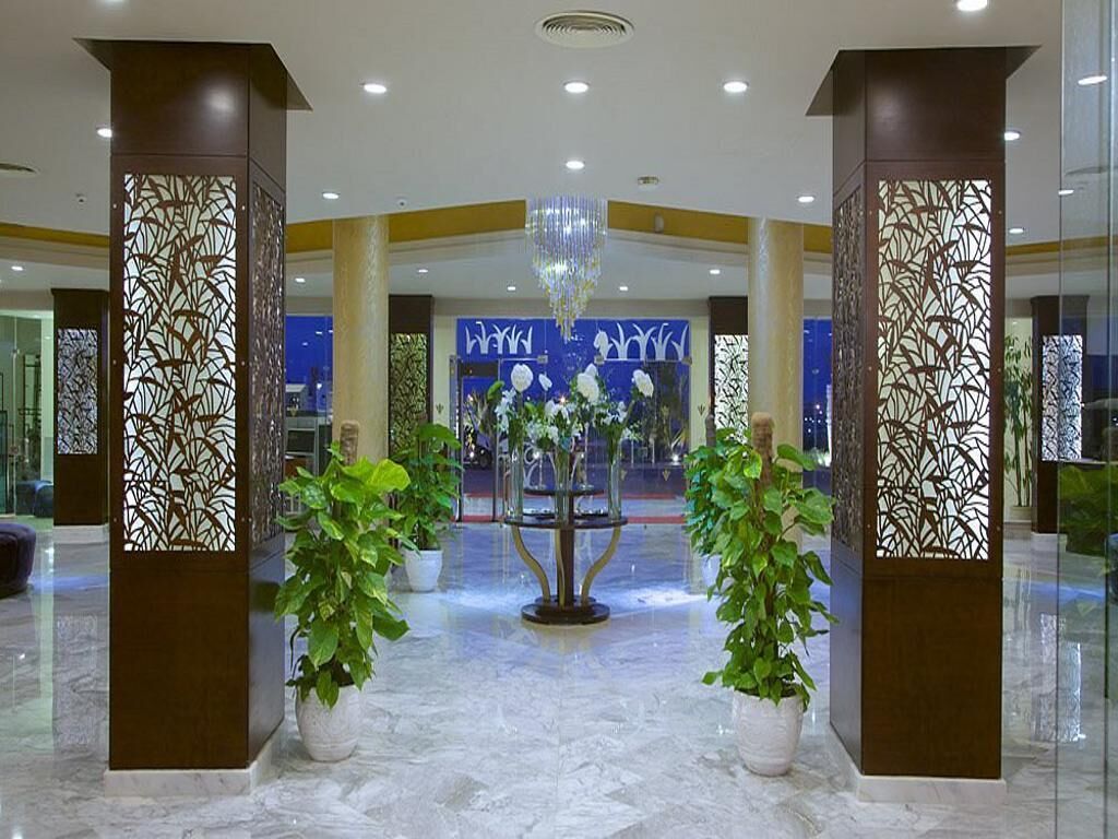 A lobby with a marble floor, decorative pillars, a chandelier, and potted plants.