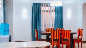 Comedor con una mesa redonda y seis sillas a rayas, un dispensador de agua y una araña.