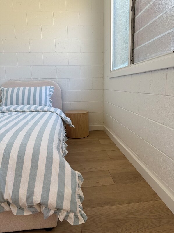 Un dormitorio con cama, ventana y suelo de madera.