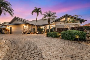 A modern house with a stone facade, a paved driveway, and palm trees.