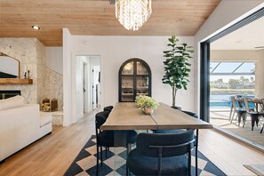 A dining area with a wooden table, black chairs, a chandelier, and a view of a pool.