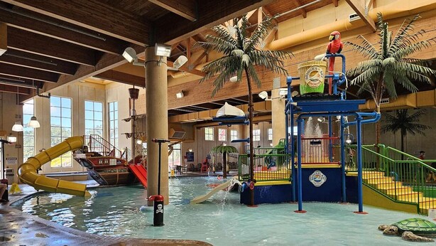 Parque acuático interior con tobogán, estructuras de juego y piscina.