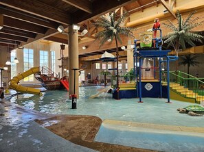 An indoor water park with a slide, play structures, and a pool.