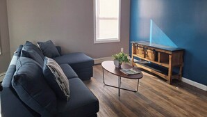 A living room with a dark blue sofa, a wooden coffee table, and a blue accent wall. - The Duo-Loft at Mt. Pleasant 2BR, Laundry, Parking (Providence)