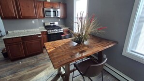 Una cocina con armarios de madera, un microondas de acero inoxidable, una estufa a gas y una mesa de comedor con sillas.