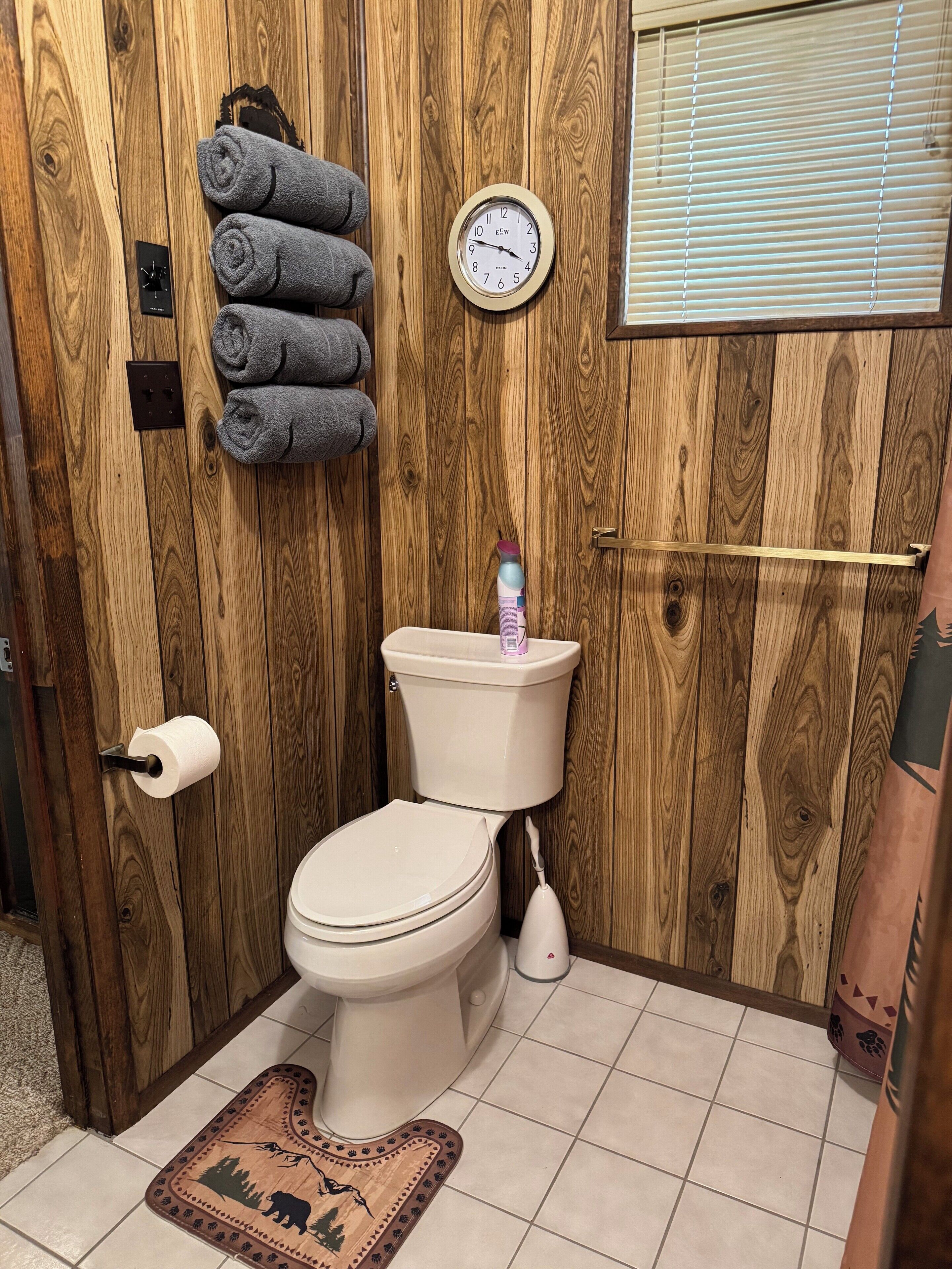 Une salle de bain avec un mur en bois, des toilettes, une horloge murale et un porte-serviettes avec des serviettes.