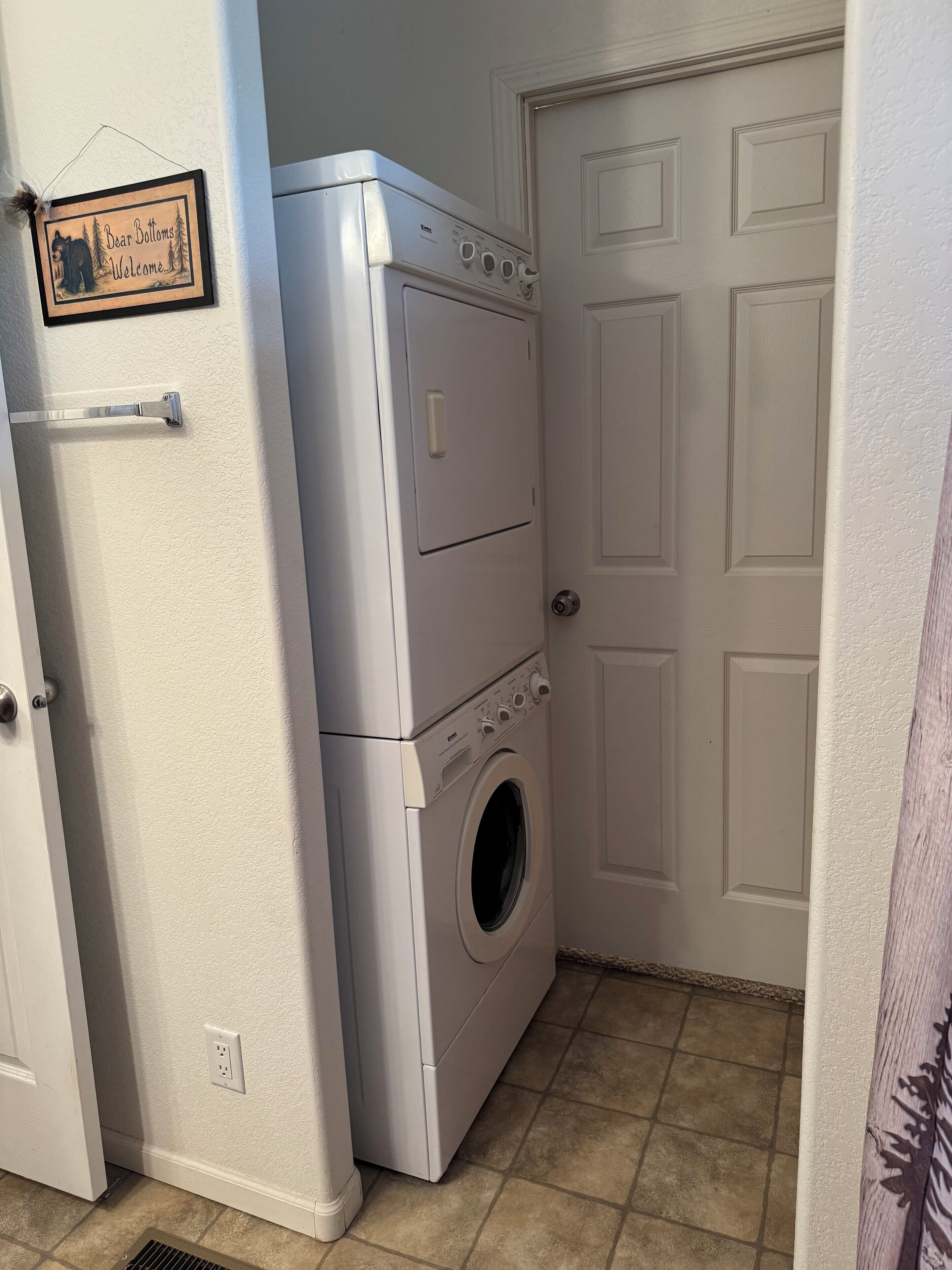 A laundry room with stacked washer and dryer units, a door, and a wall-mounted sign.