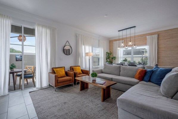 Uma sala de estar moderna com um sofá, duas poltronas, uma mesa de centro e um espaço de jantar com mesa e cadeiras.