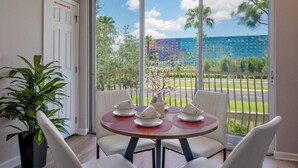 A dining area with a table set for four, a potted plant, and a view of a building with a colorful facade. - TH14 - 3BR house with pool access near Disney (Orlando)