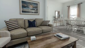 A living room with a beige sofa, a coffee table, and a dining area with white chairs and a table.