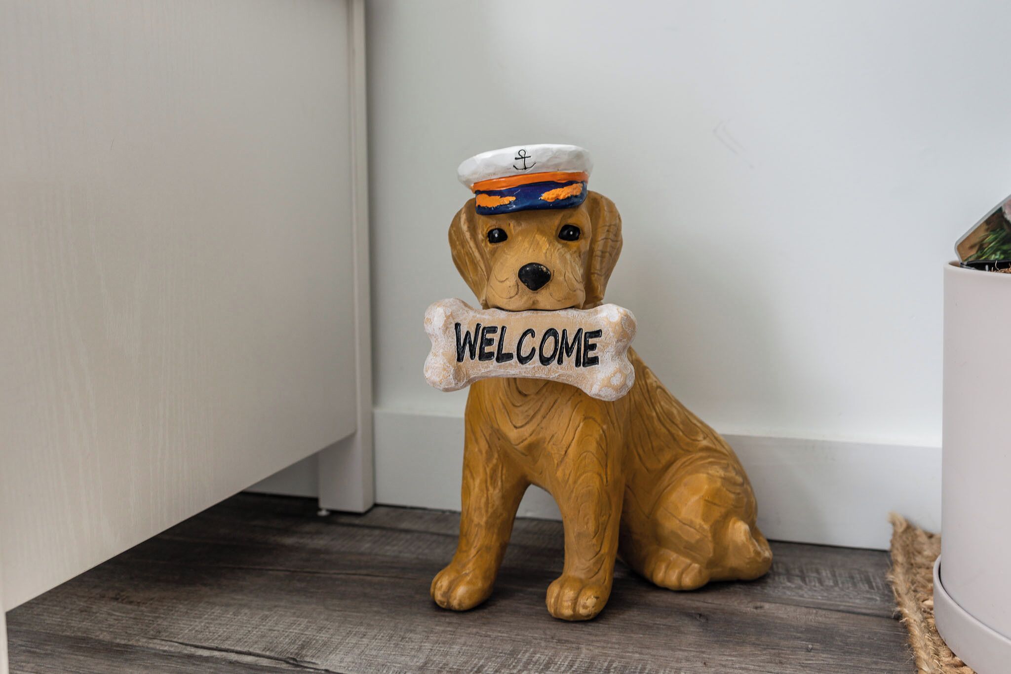 Uma figura de cão de madeira com chapéu de marinheiro e uma placa com a palavra 'WELCOME'.