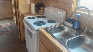 A compact kitchen with a white stove, a sink, and wooden cabinets. - Custom built cool cabin with AC in Holiday Beach. Not a converted shed. (Rockport)