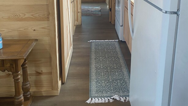 A narrow wooden hallway with a refrigerator, a small table, and a rug leading to a door. - Custom built cool cabin with AC in Holiday Beach. Not a converted shed. (Rockport)