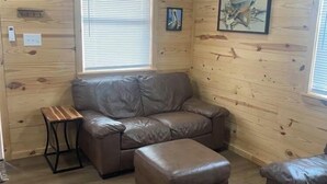 A cozy room with wooden walls, a leather sofa, an ottoman, and a small table. - Custom built cool cabin with AC in Holiday Beach. Not a converted shed. (Rockport)