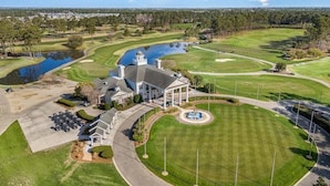 A golf course with a clubhouse, a pond, and a parking area.