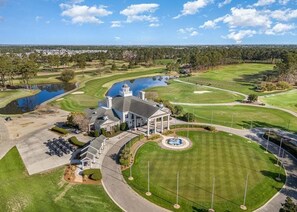 A golf course with a clubhouse, a pond, and a parking area. - NEWLY RENOVATED 2BR Golfer's Paradise Condo at World Tour (Myrtle Beach)