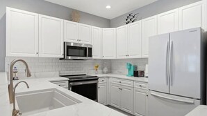A modern kitchen with white cabinets, a stainless steel refrigerator, a microwave, and a sink. - NEWLY RENOVATED 2BR Golfer's Paradise Condo at World Tour (Myrtle Beach)