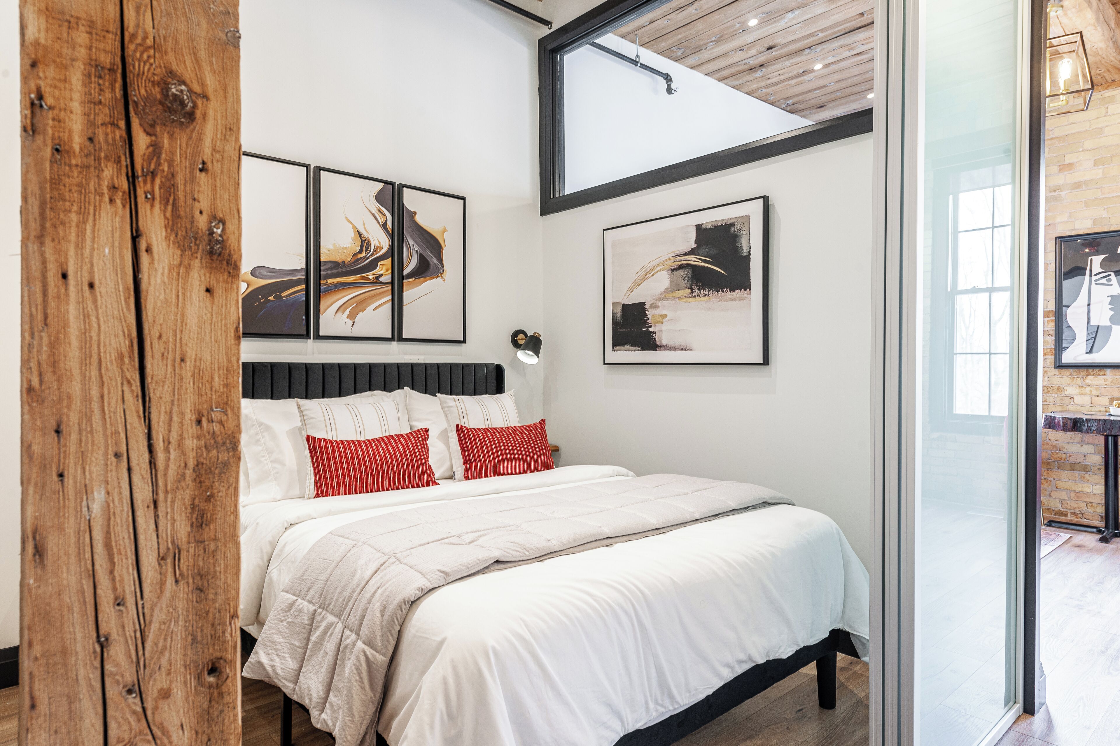 Quarto moderno com uma cama grande, vigas de madeira e obras de arte nas paredes.