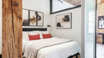 Quarto moderno com uma cama grande, vigas de madeira e obras de arte nas paredes.