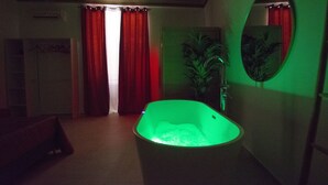 Une salle de bain avec une baignoire éclairée de lumière verte, des rideaux rouges et un miroir au mur.