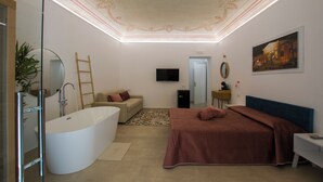 Une chambre à coucher moderne avec un grand lit, une baignoire, un téléviseur et un tableau au mur.
