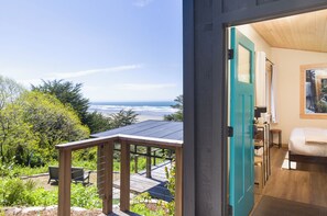Une pièce avec vue sur l’océan, une terrasse en bois et une porte de couleur turquoise.