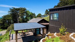 A modern house with a covered patio, a small garden, and a view of the surrounding forest.