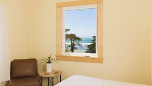 A bedroom with a large window overlooking a beach, a brown leather chair, and a small round table with a plant.