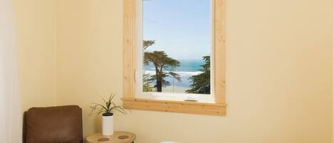 A bedroom with a large window overlooking a beach, a brown leather chair, and a small round table with a plant.
