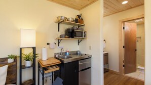 A compact kitchen with a refrigerator, microwave, and shelves with kitchenware.