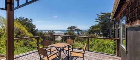 A wooden deck with a table and chairs, overlooking a beach and ocean.