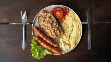 Un plato con tostadas, frijoles, salchicha, tomates, lechuga y huevos revueltos sobre una mesa de madera.